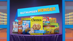 Still of bannered sample table in grocery store from Nashville based Outnumber Hunger 2016 TV Spot animated by Nashville's ST8MNT employing a large grocery store automatic glass door entrance with a sample table full of Fiber One, Hamburger Helper, Nature Valley, Pillsbury, Cheerios, Lucky Charms, Suddenly Salad, Old El Paso and Reese's Puffs