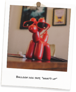 Polaroid of red balloon dog with caption "Balloon Dog says What's up"