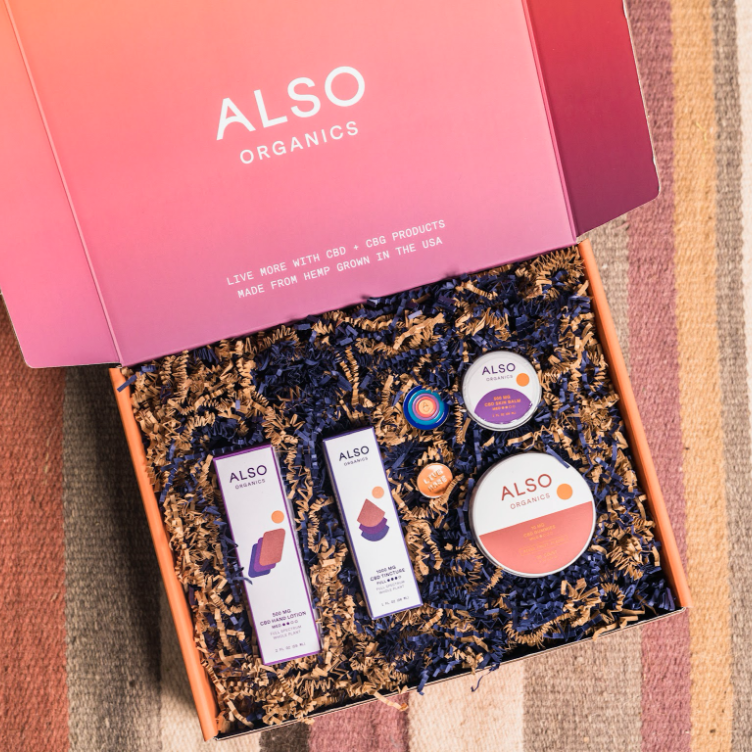Opened influencer kit featuring several Also Organics CBD products and branded enamel pins