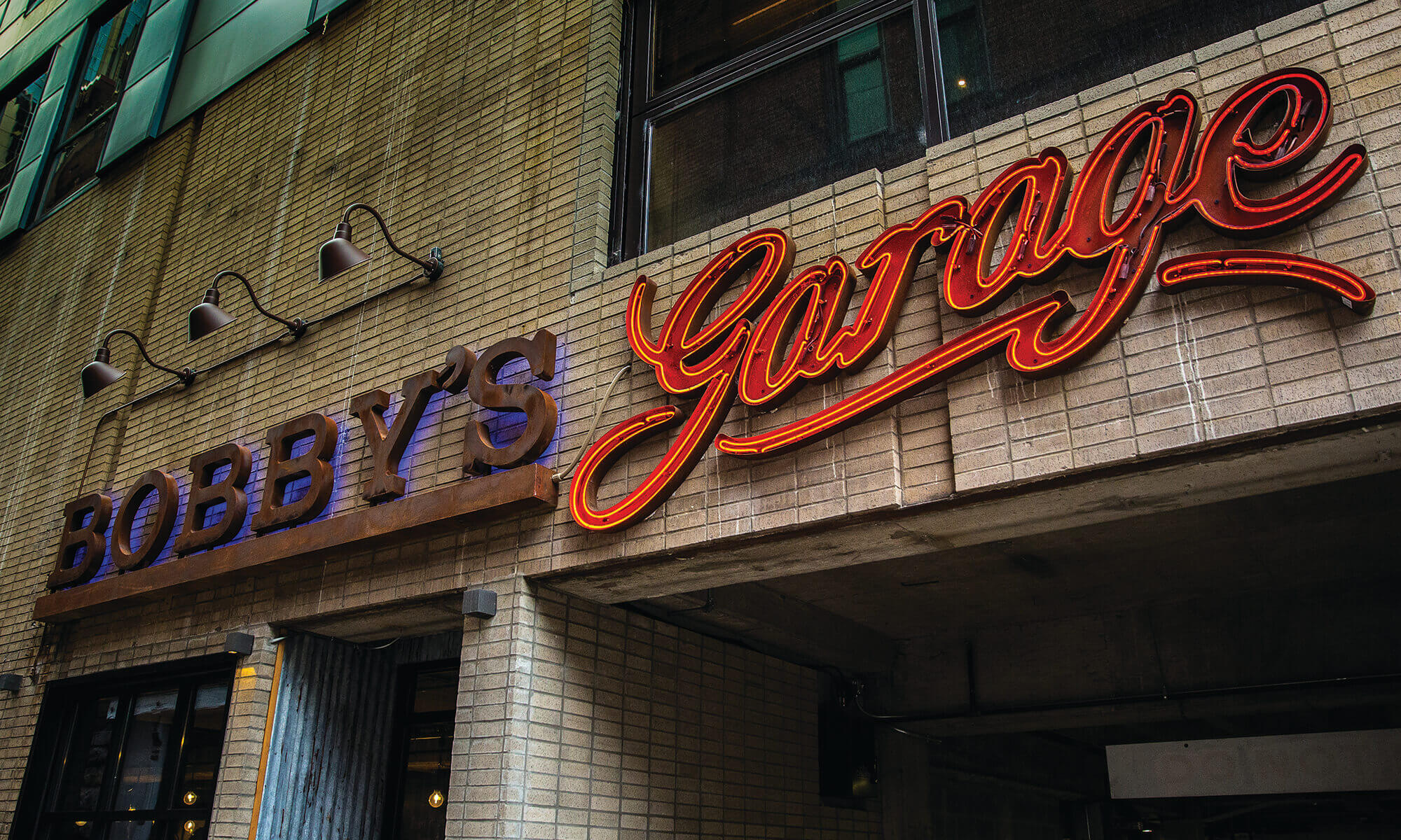 neon and metal Bobby's Garage logotype sign on a brick wall above a door and garage entrance