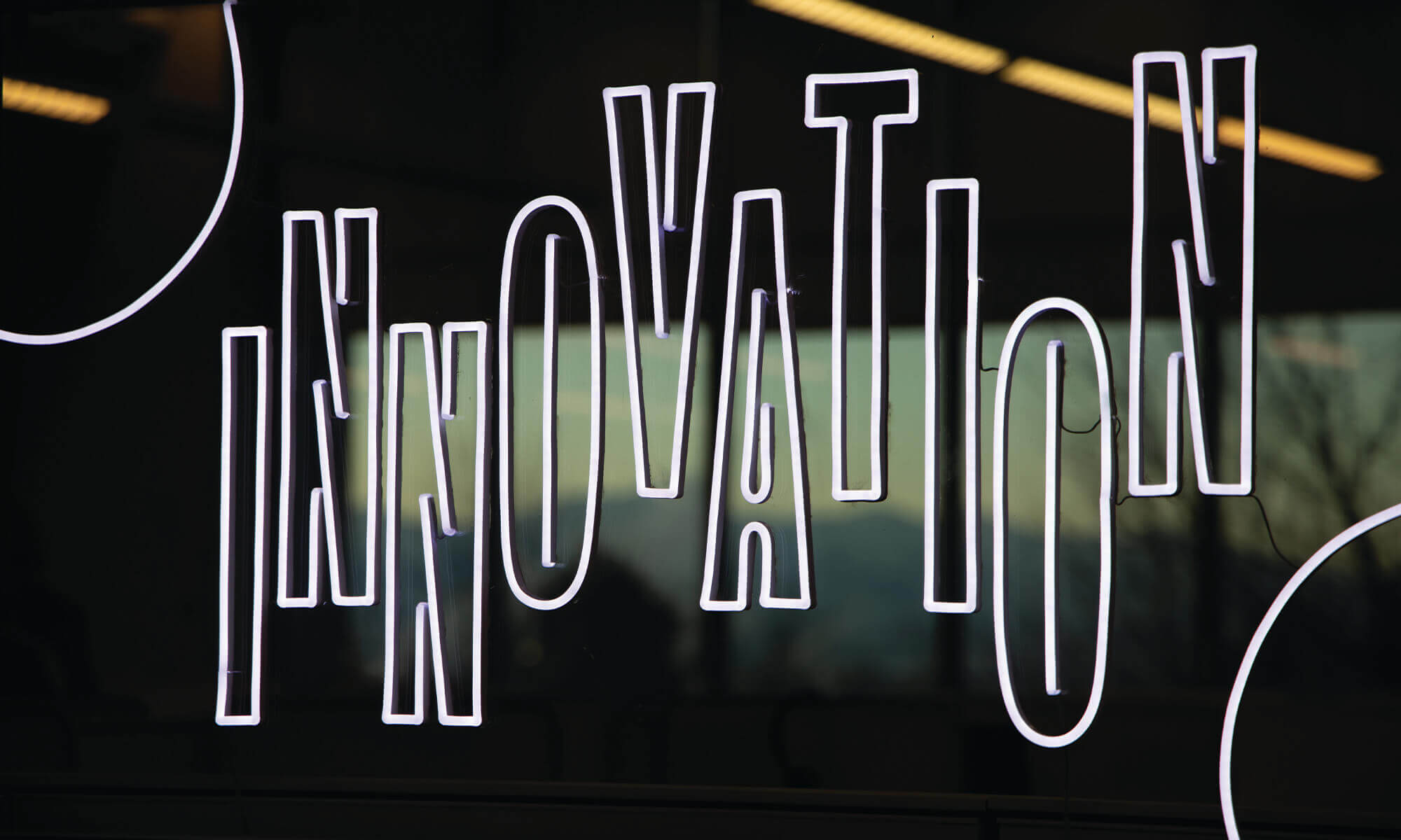 White LED tubing letterforms spelling out the word INNOVATION on glass panel with background reflections