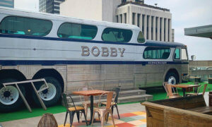 Greyhound bus sitting on a rooftop bar with BOBBY painting on side