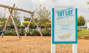 Acrylic vibrant aqua and white Tot Lot sign with playground rules and swing set in background