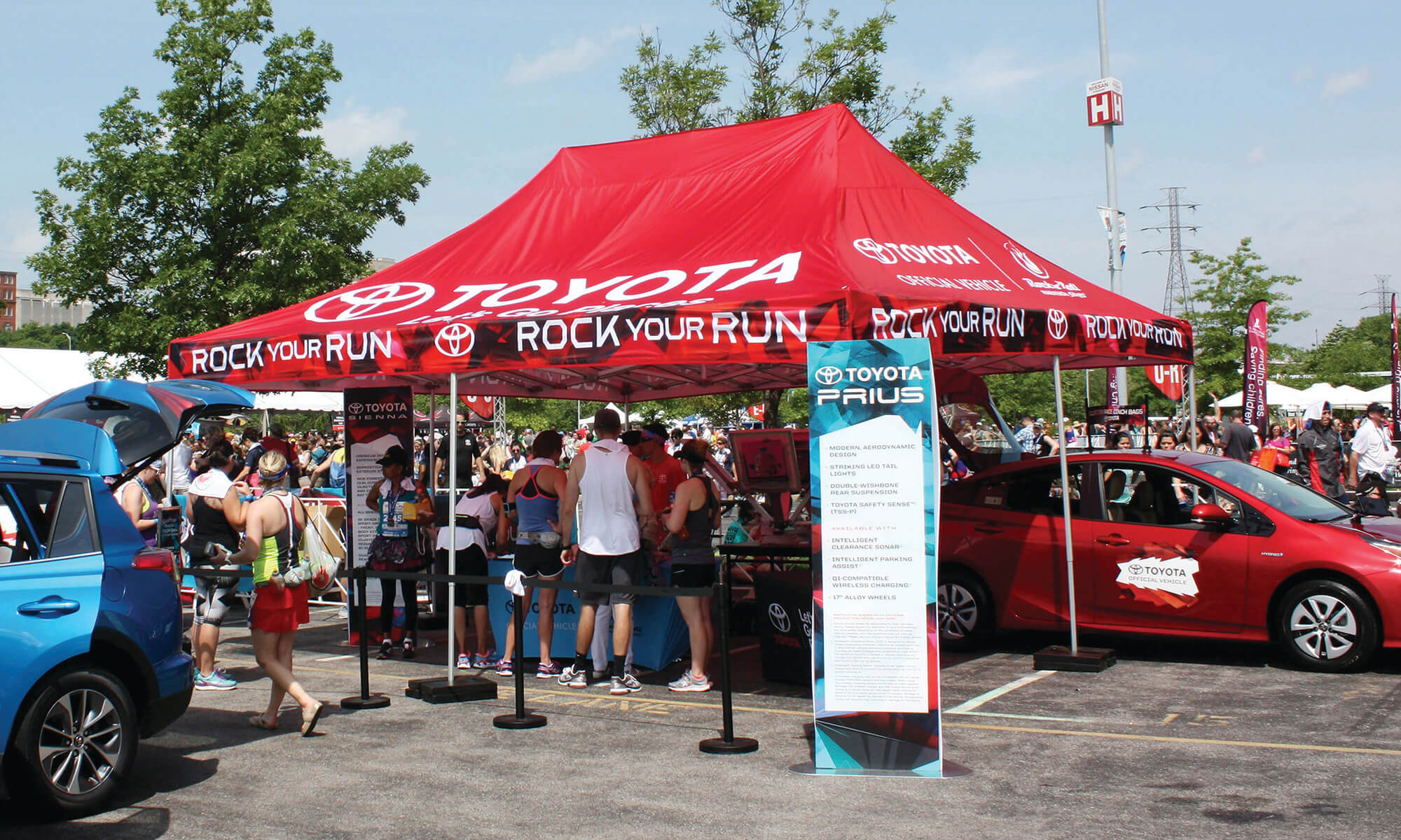 Red tent top with people standing underneath and Prius standee event signage for Toyota Rock Your Run