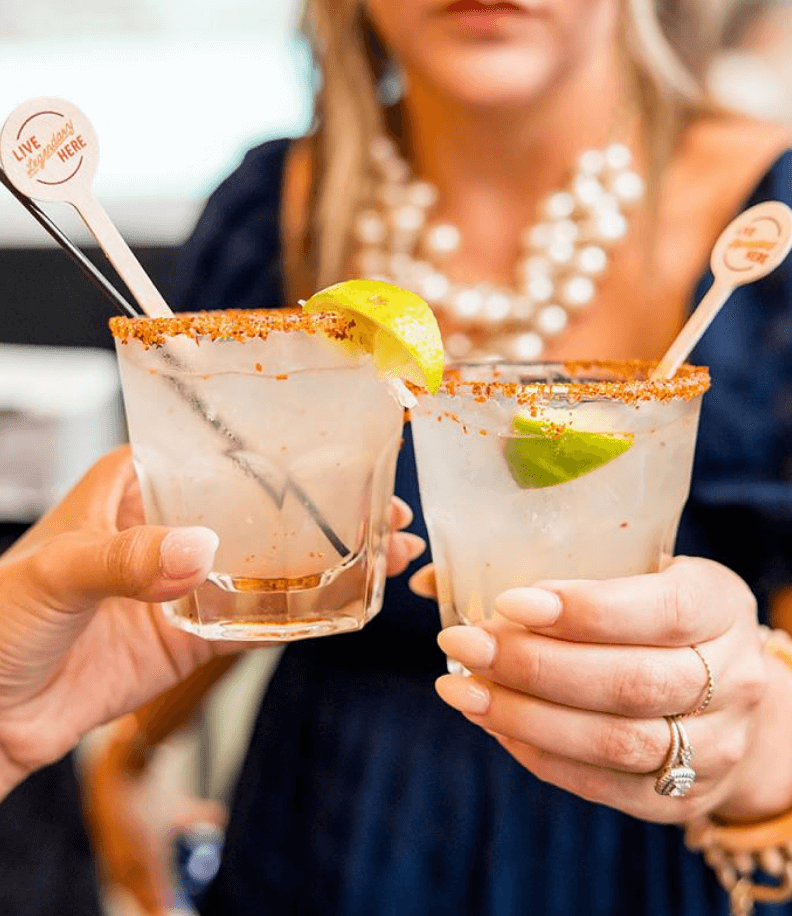Image of two margarita glasses cheersing with branded drink stirrers from the name reveal event