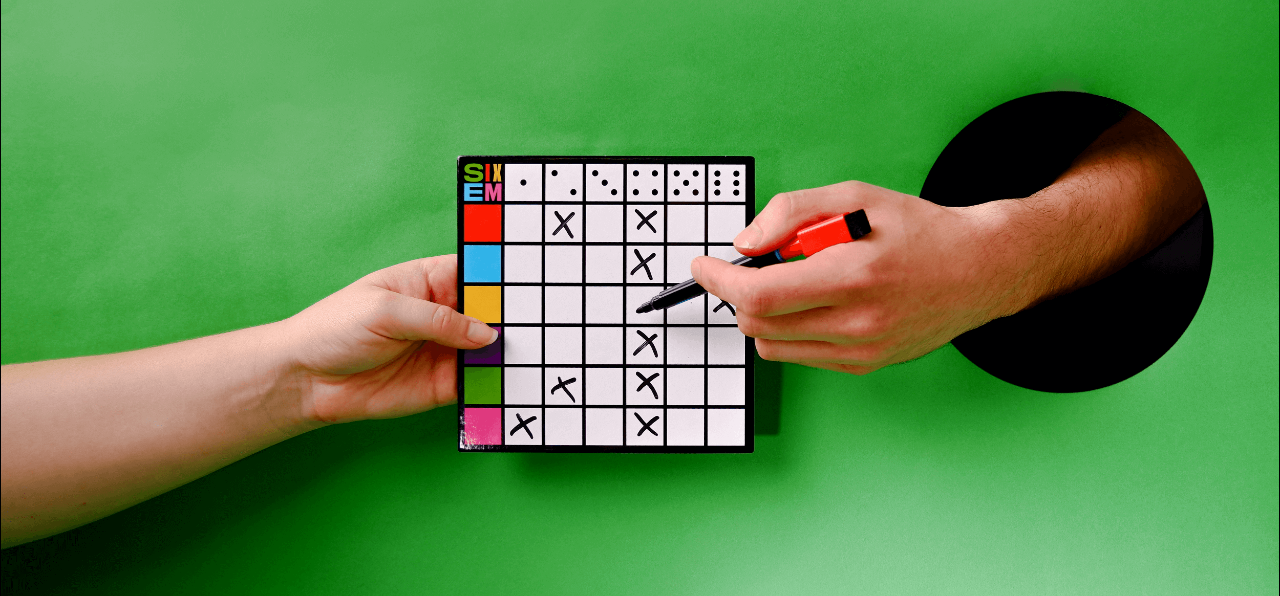 SIXEM dry erase board being held in the center of the image by one arm coming in from the left while another sticks out from a hole in the green background while holding a marker