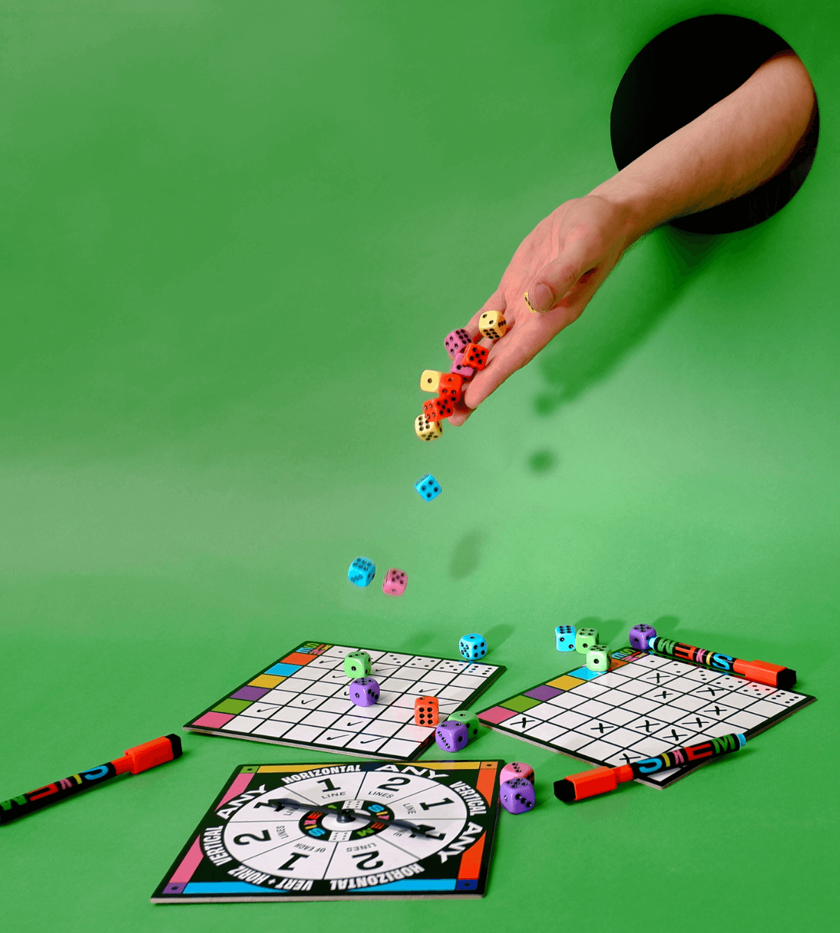 A hand sticks out from a hole in the green background and tosses dice in motion onto game pieces below