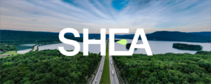 SHEA monogram logo laid over an image of a road and lakes