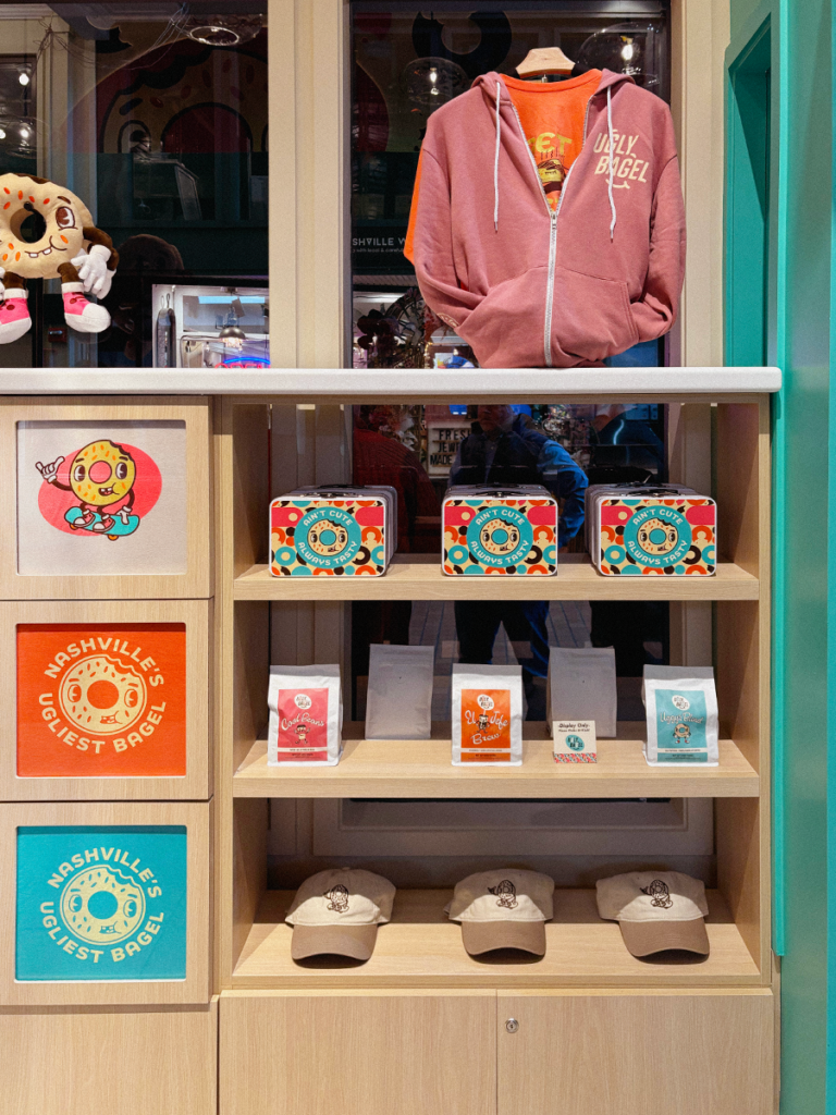 View of Ugly Bagel merch corner shelves with hats, shirts, and coffee