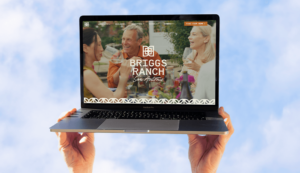 Hands holding laptop against blue sky with Briggs Ranch home page header design showcasing logo by ST8MNT